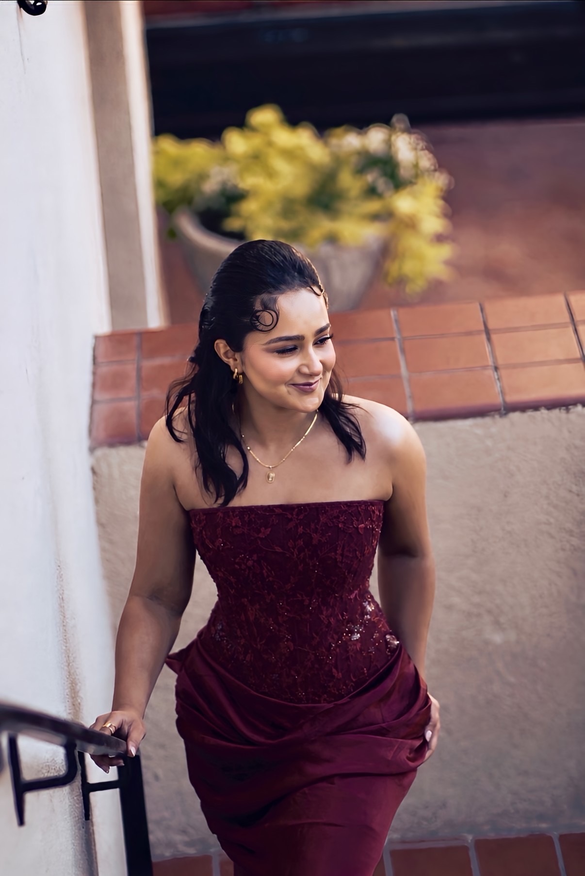 Keziah Salman smiling in a burgundy evening gown by a staircase